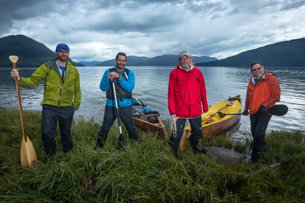 4 people standing in front of a lake with canoes
