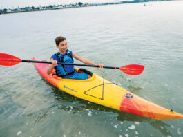 Young boy paddling orange and yellow kayak