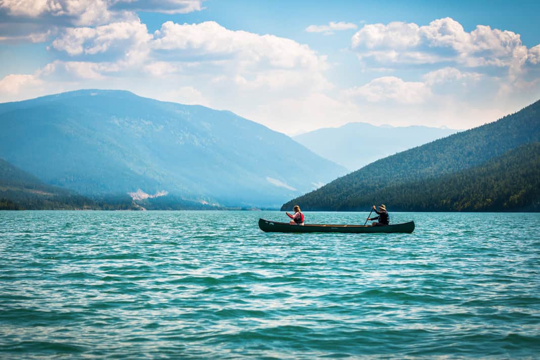 two people paddling a canoe on Lake Revelstoke surrounded by mountains