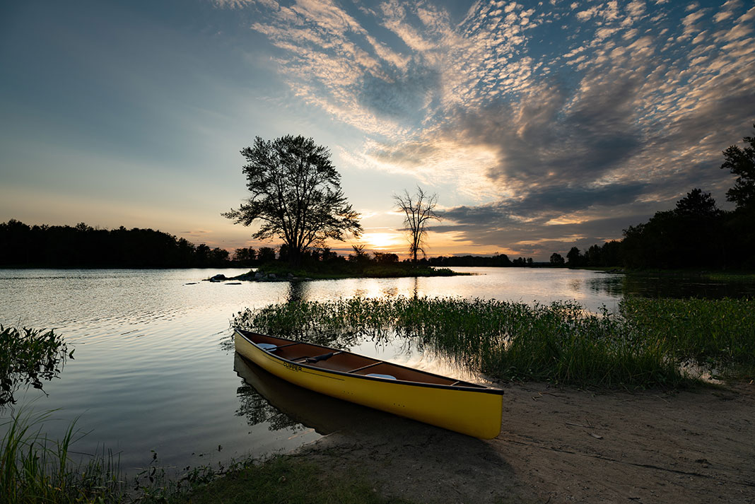 a canoe with design features borrowed from the racing world sits on a sandy bank at dusk