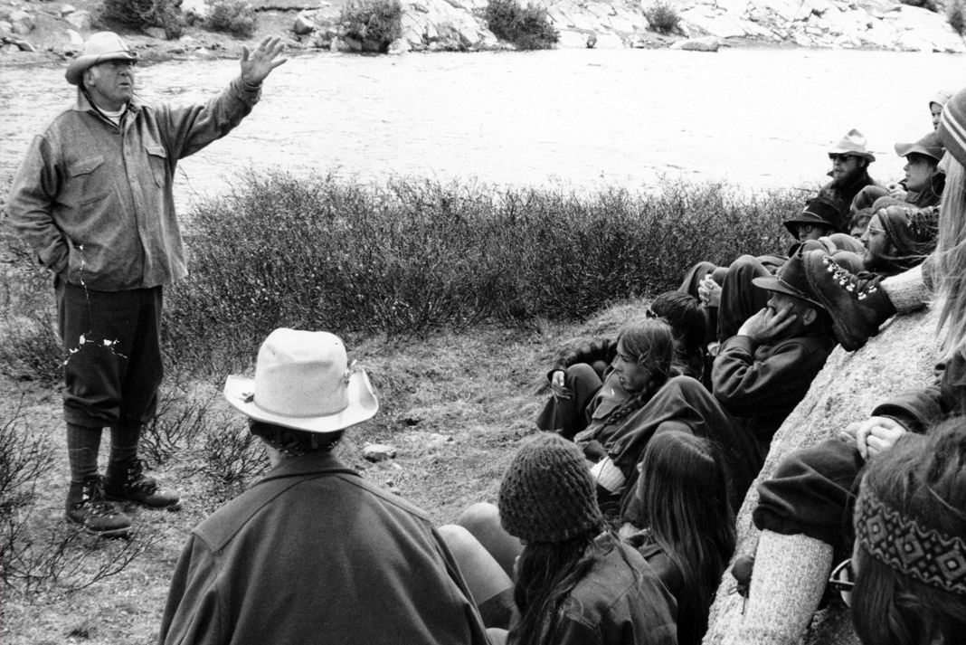 Paul Petzoldt talking to several paddlers in front of a lake