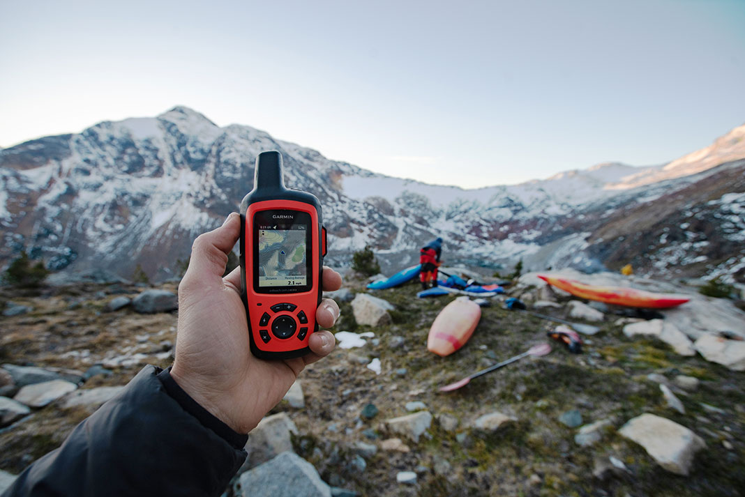 person holds up a Garmin handheld GPS at a mountainous kayak location