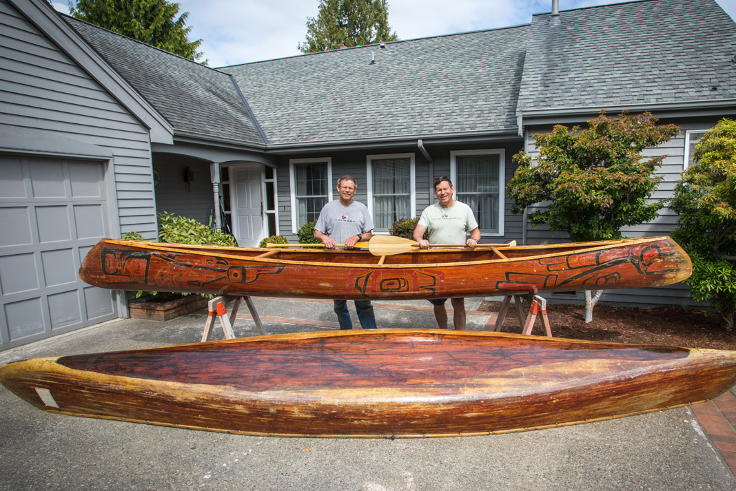 two mend standing behind two canoes