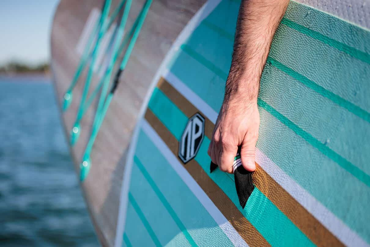close-up of a man holding the grab handle on an inflatable SUP while carrying it