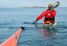 a person paddles toward an island while towing another sea kayak