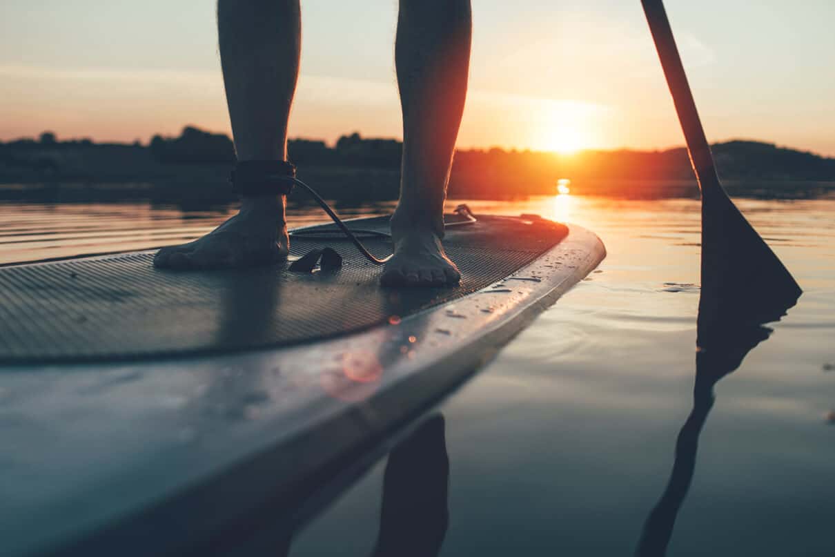close up on feet and board of person paddleboarding at dusk