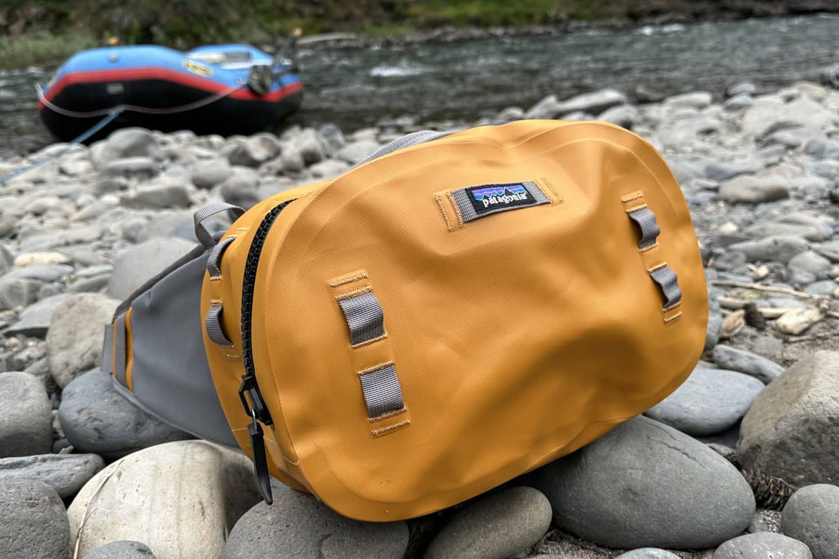 The Patagonia Guidewater waterproof hip pack sitting on rocks near the edge of a river with a raft in the background.