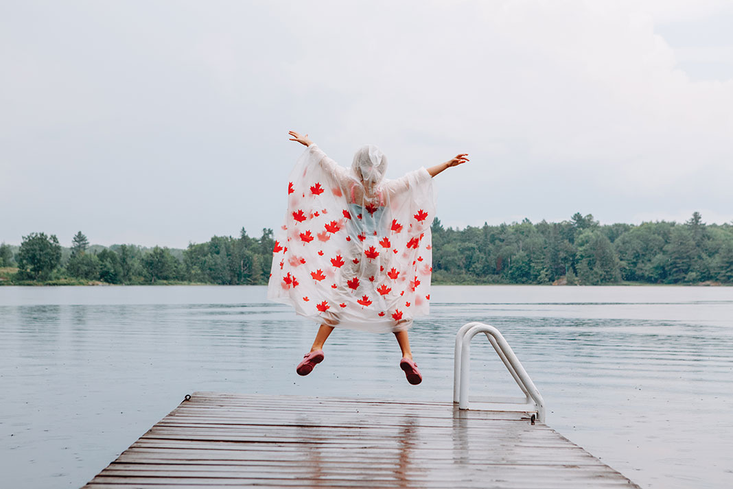 a person jumping at the end of a dock while wearing a maple leaf poncho in rainy weather