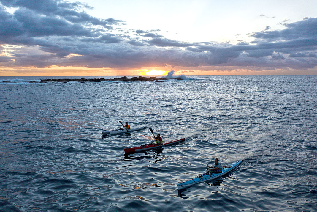 three sea kayakers paddle across the Bass Strait at dusk