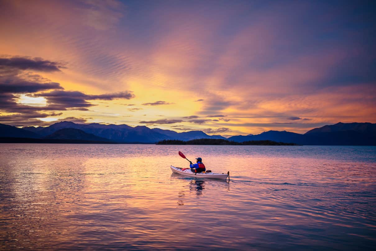 A kayaker paddles on calm water at dusk