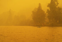 a paddler kayaks in the hazy yellow wildfire light of the summer season