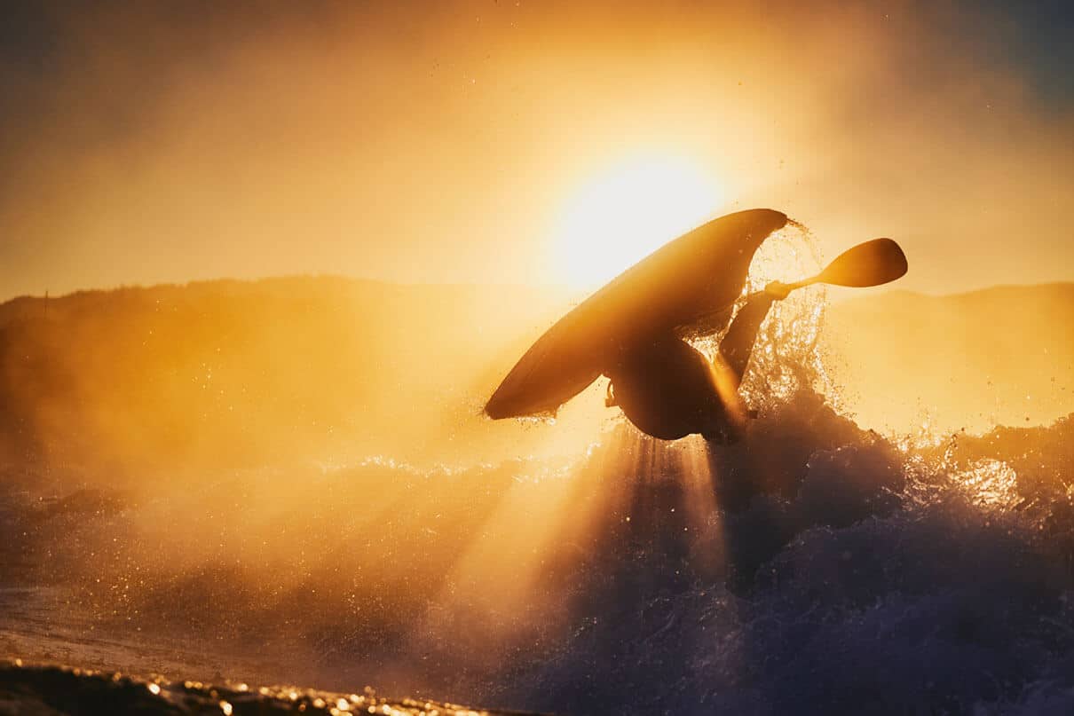 freestyle kayaker is silhouetted by the rising sun during a sunrise kayaking photography session