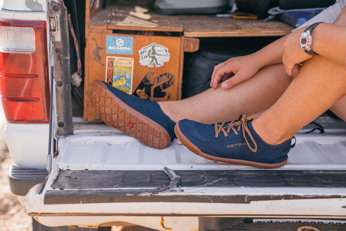 A person sits on a tailgate wearing Astral Loyak water shoes.