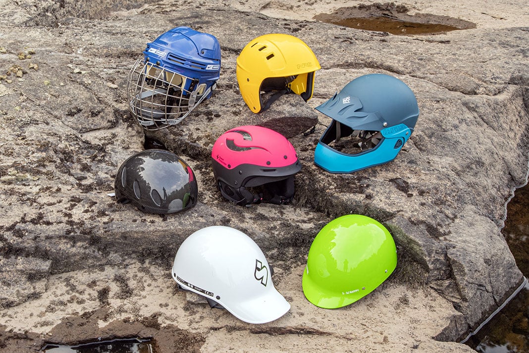 a selection of whitewater helmets are arranged on a river rock