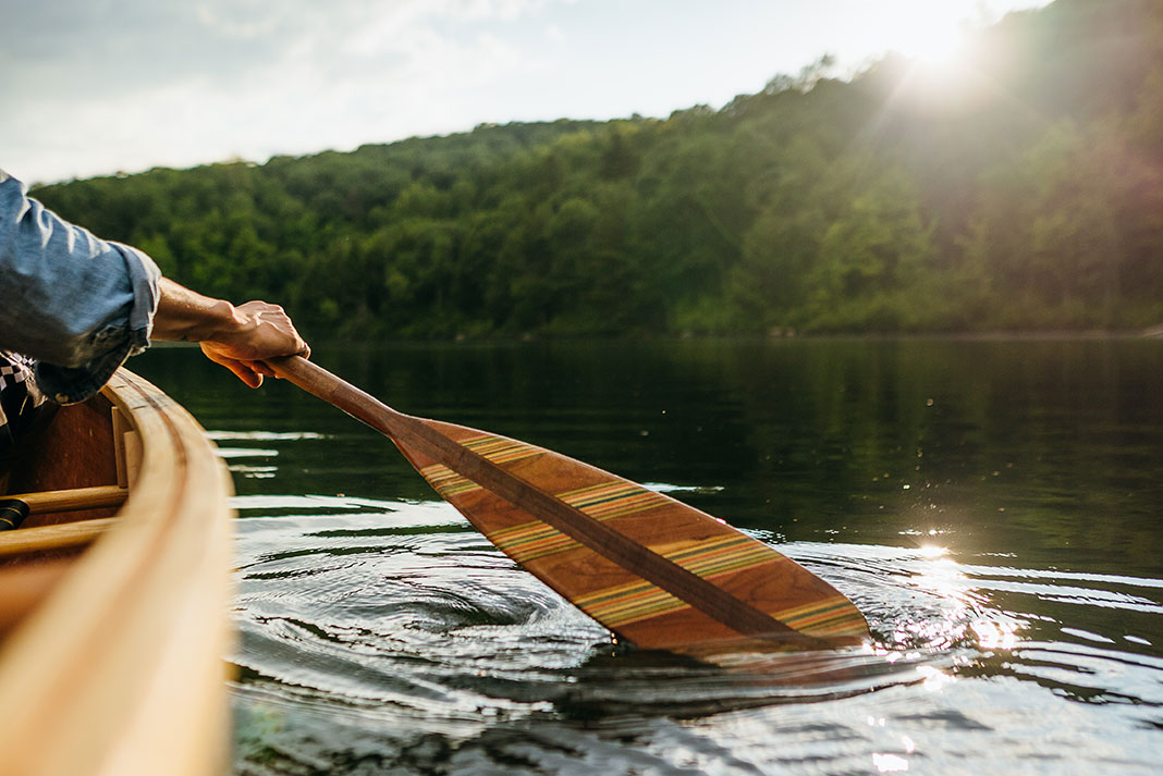 person paddles a canoe with a wooden paddle
